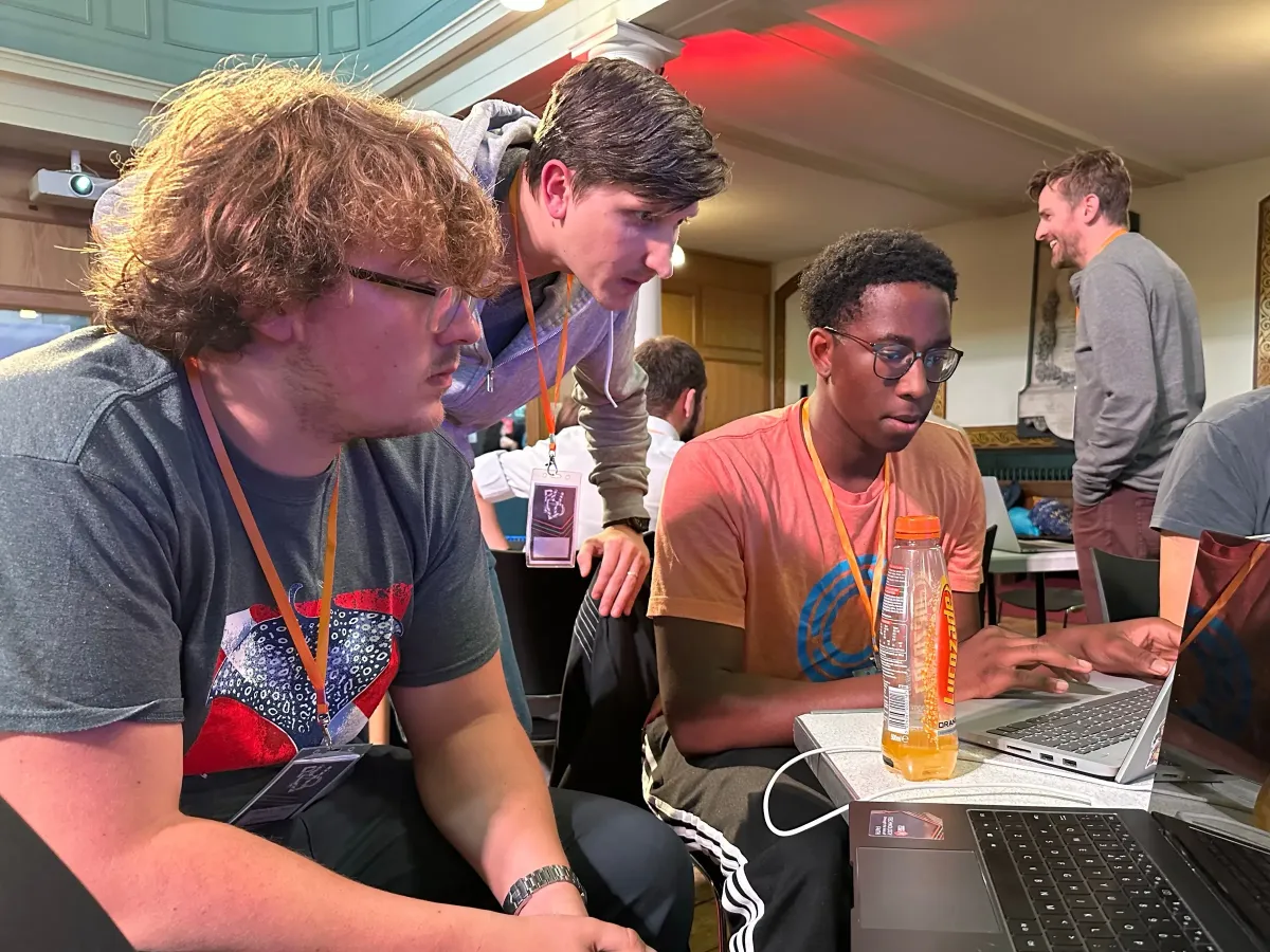 Three builders gathered around a laptop at a past BUILD weekend