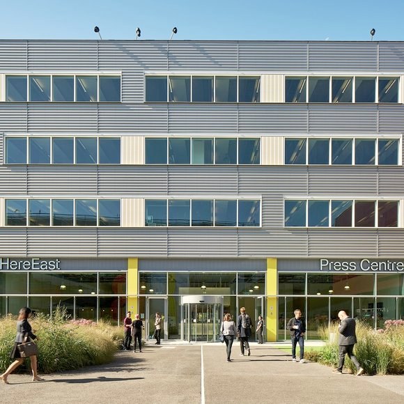 The Press Centre entrance at Here East: a revolving door between two yellow pillars, under the Press Centre sign